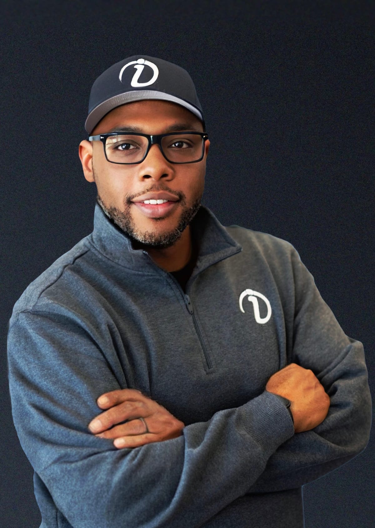 Dante Walston, arms crossed, wearing an IntegrateU quarter-zip and cap